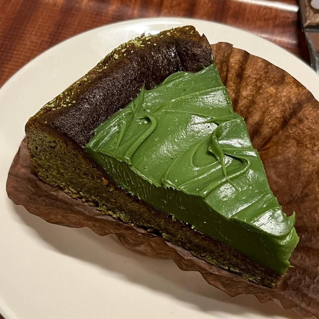Slice of matcha Basque cheesecake with glossy green topping on a white plate