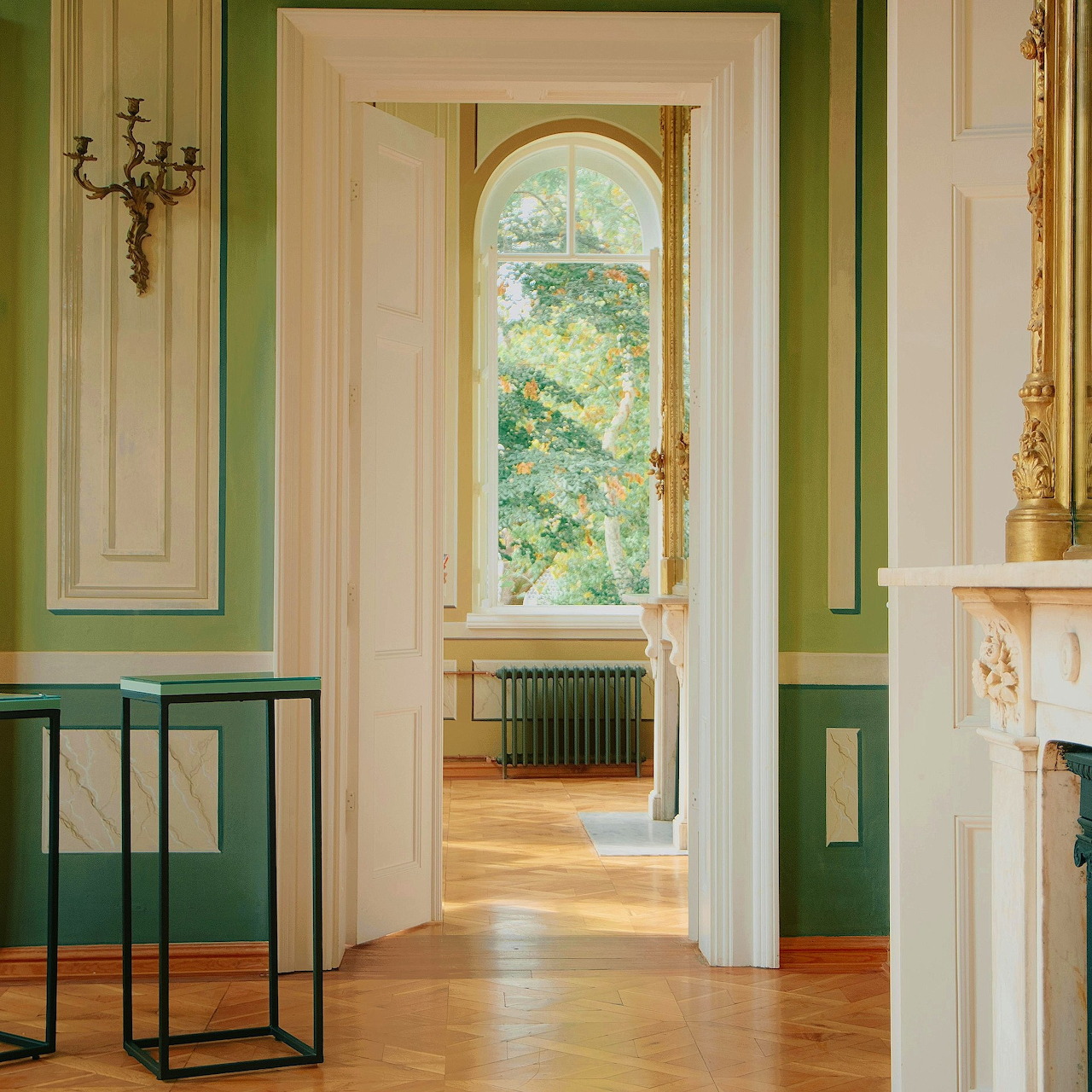 Open white interior doors leading to a bright room with green walls, wood floor, and arched window