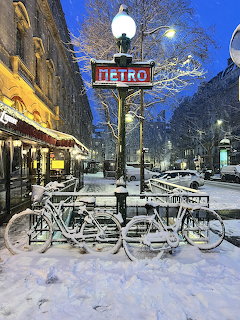 Snow-covered Paris Metro sign and bicycles on a wintry Parisian street at dusk