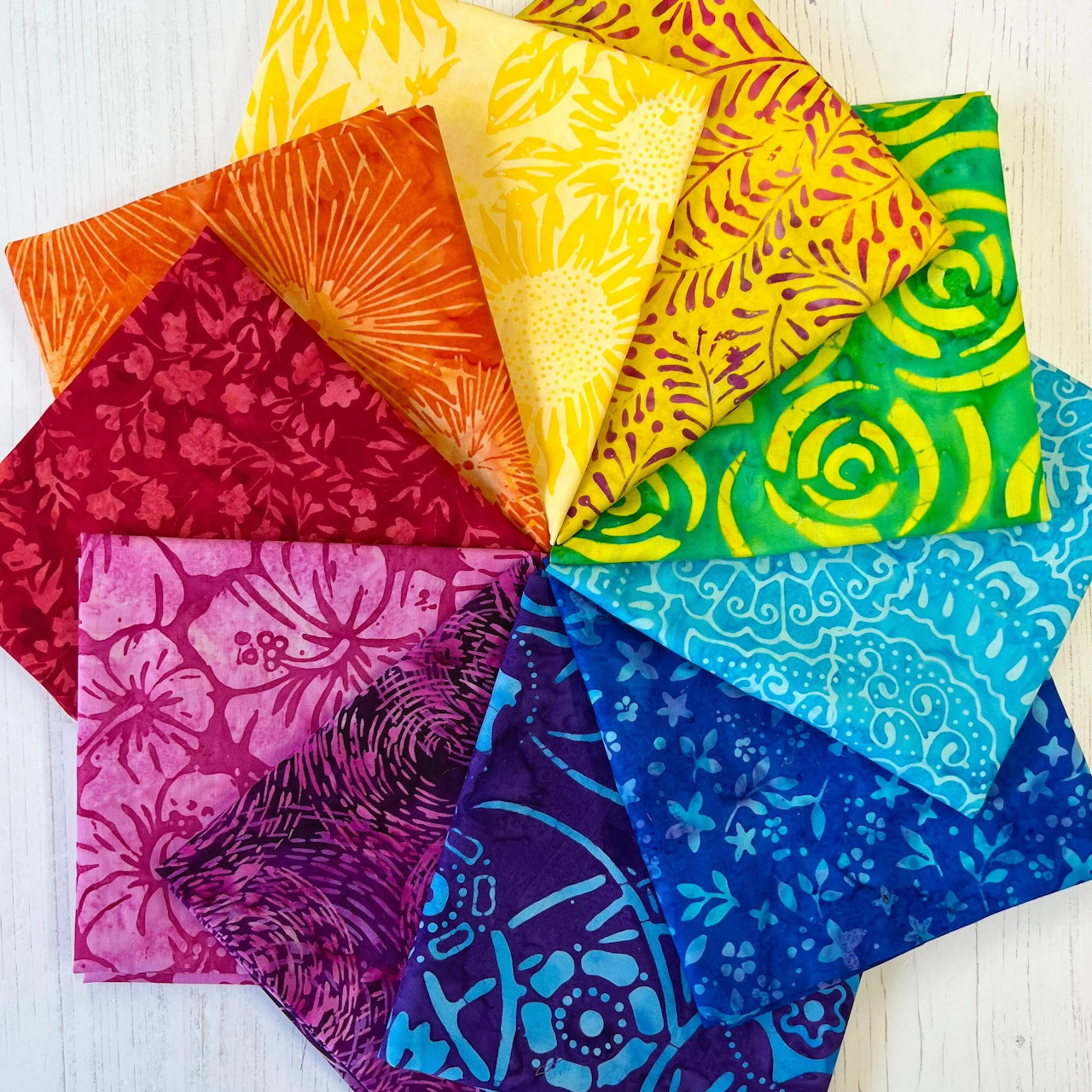 Colorful batik fabric swatches arranged in rainbow spectrum with decorative patterns