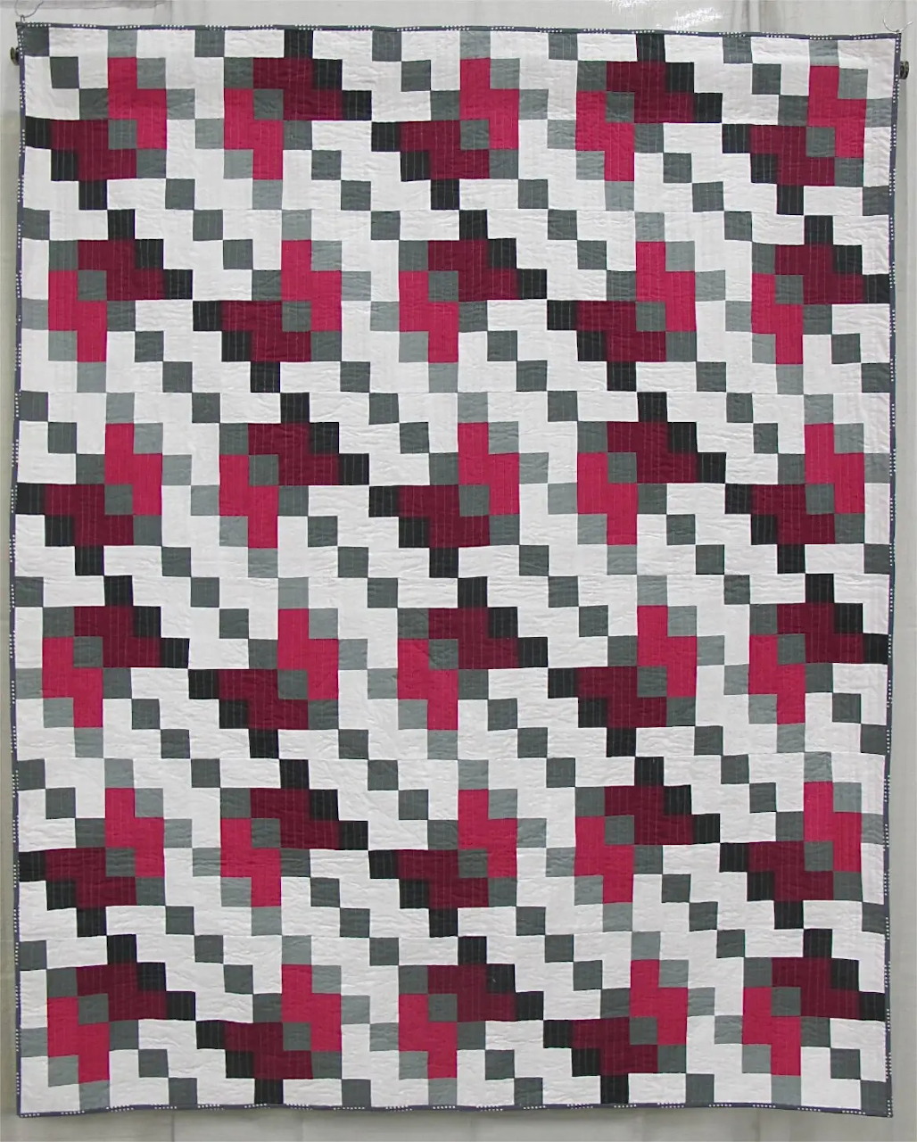 Geometric quilt with diagonal pink and gray blocks on checkered background