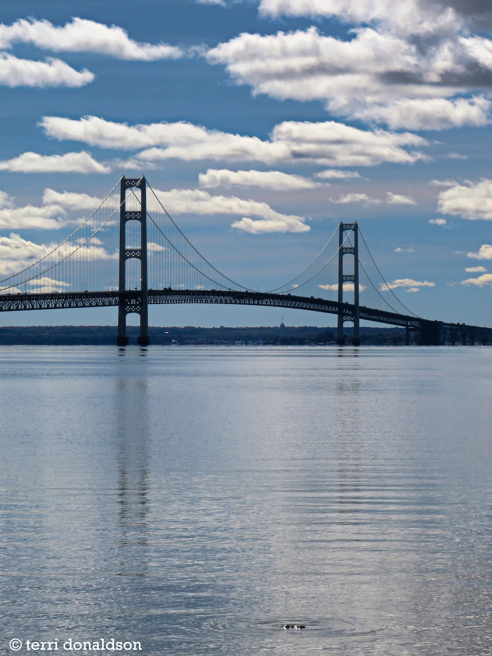 Suspension bridge over calm water beneath a blue sky with scattered white clouds