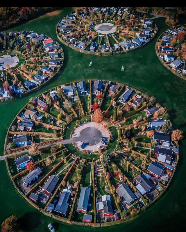 Aerial view of circular housing developments with colorful homes arranged in rings, surrounded by green water in Copenhagen
