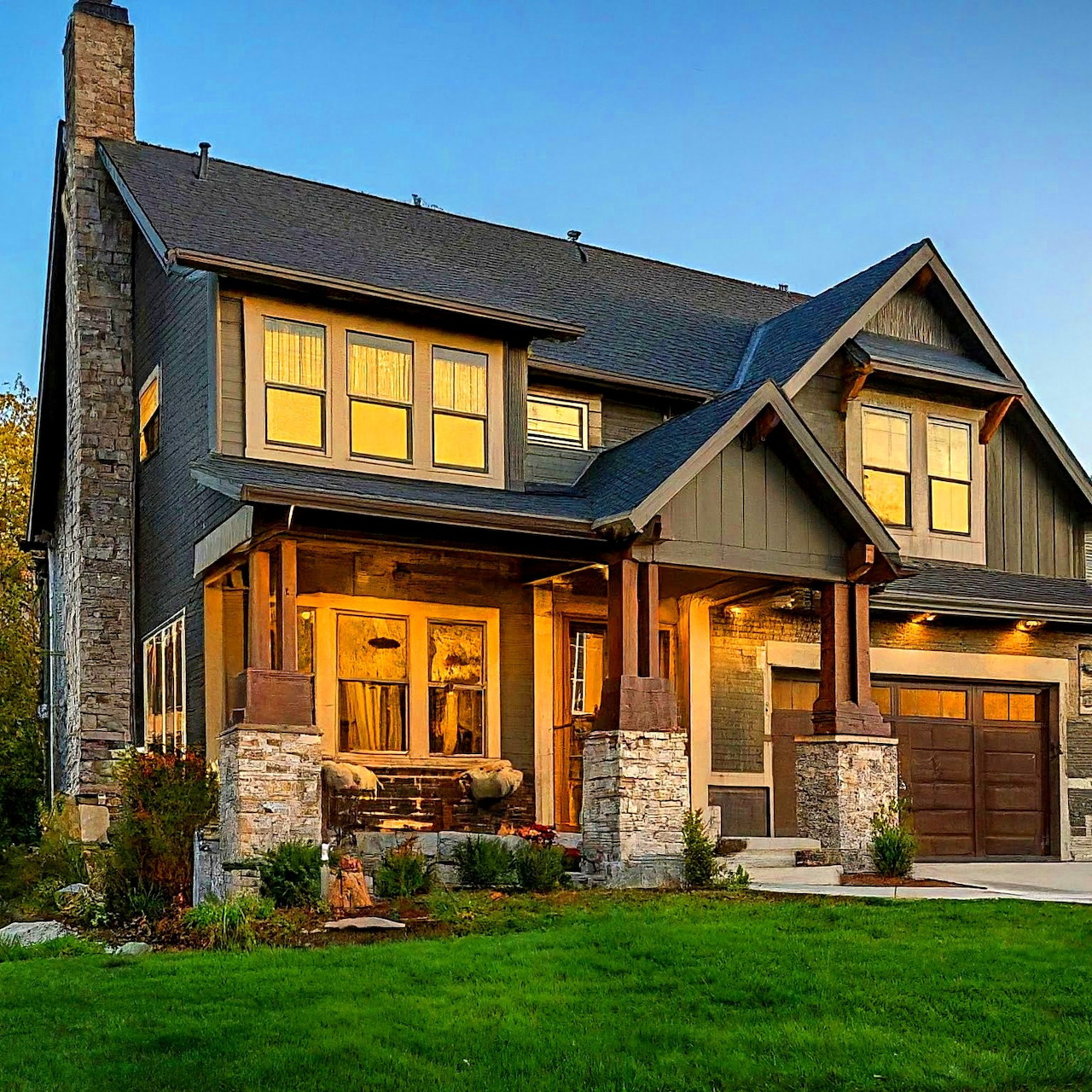 Craftsman-style house with lit windows and stone accents at twilight