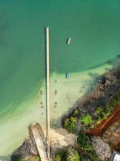 Aerial view of a wooden pier stretching into clear turquoise water with small boats near a sandy shore