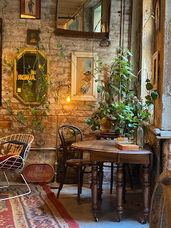Cozy coffee shop interior with brick walls, wooden tables and chairs, green plants, and warm lighting
