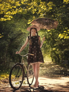 Woman in polka dot dress holding parasol and bicycle on sunny autumn path