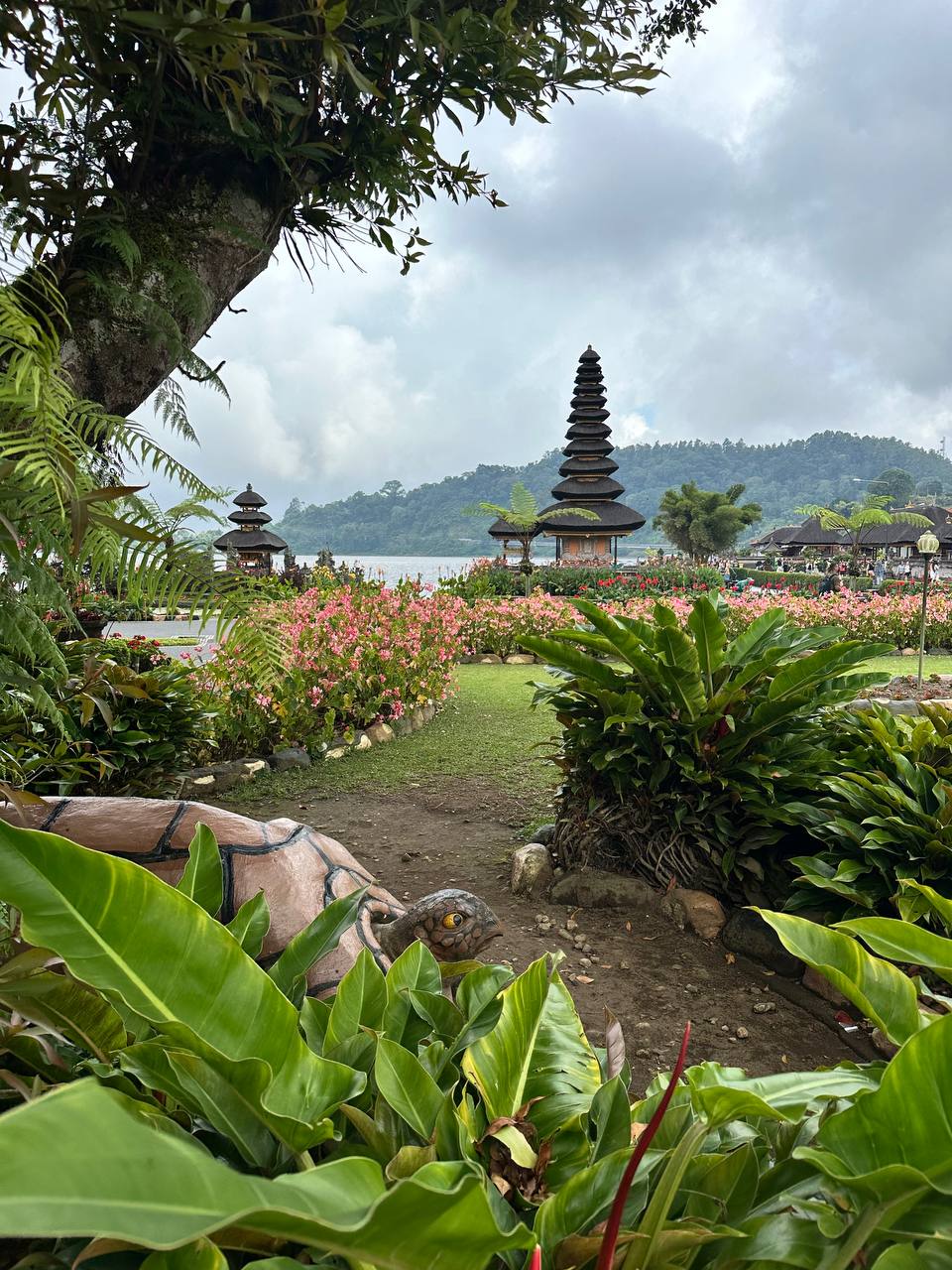 Tropical garden path leading to a traditional Balinese pagoda temple by a lake with misty mountains behind