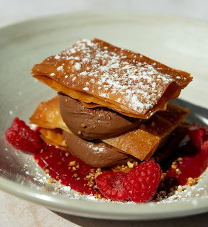 Stacked chocolate mousse dessert with wafers, raspberries, and powdered sugar