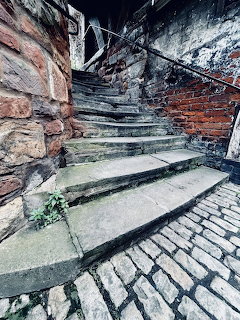 Curved old stone staircase between weathered brick and stone walls with metal handrail