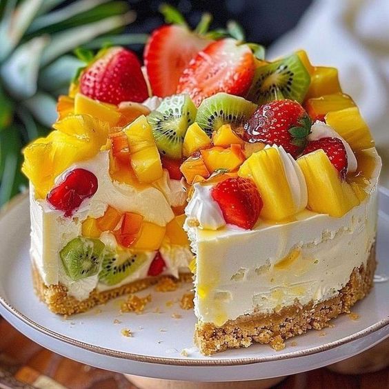 Cheesecake slice with colorful tropical fruits including strawberries, kiwi, and mango on white plate