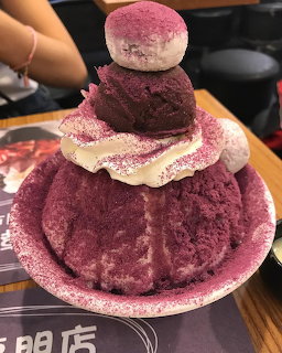 Large purple ube shaved ice dessert stacked in layers with white cream on a pink plate