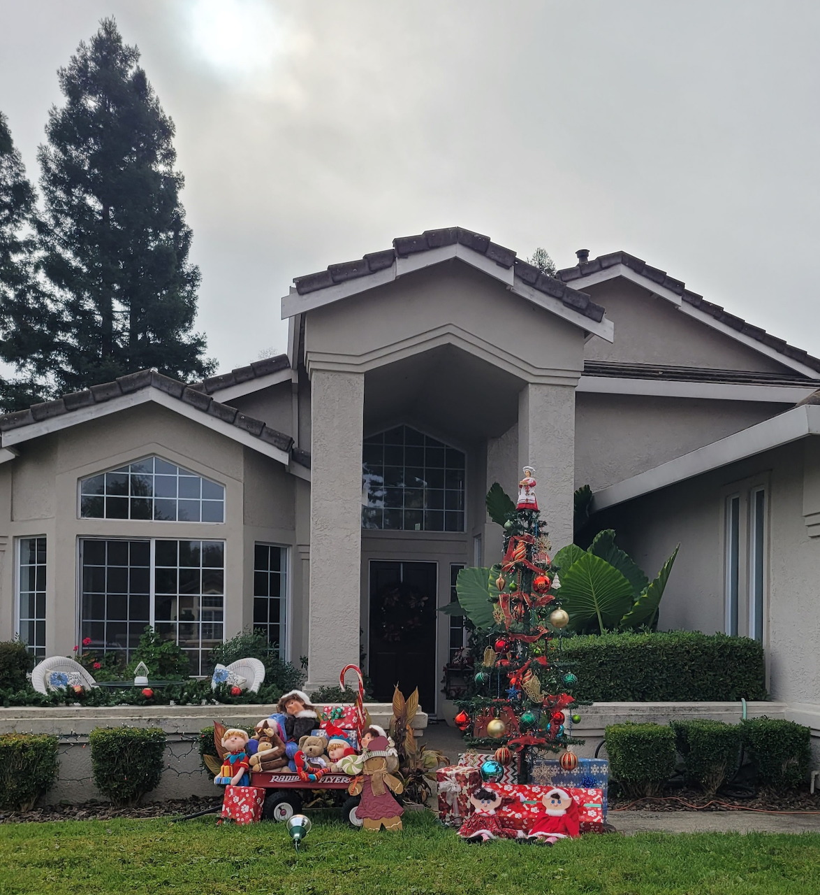 Suburban house with Christmas tree, wrapped presents, and holiday decorations on the front lawn