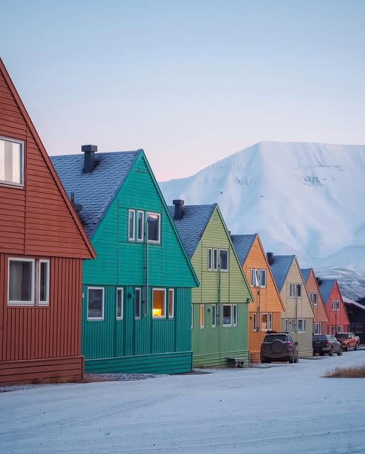 Row of colorful wooden houses in snow with mountain behind in Norway winter