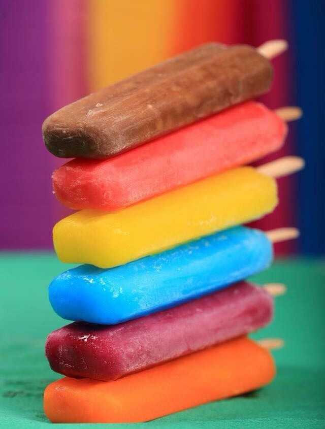Stack of colorful popsicles in rainbow colors against a multicolored striped background