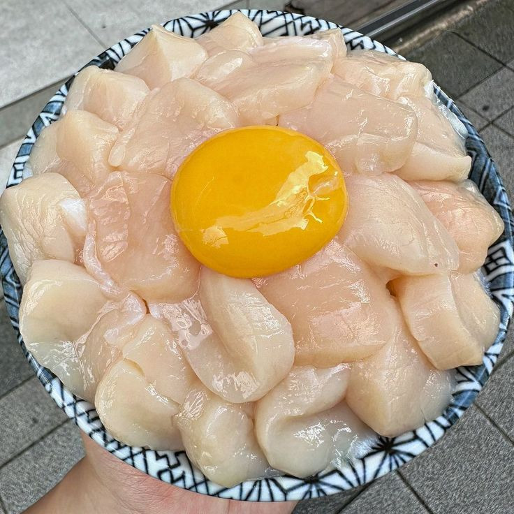 Rice bowl with raw scallop slices arranged around a central egg yolk