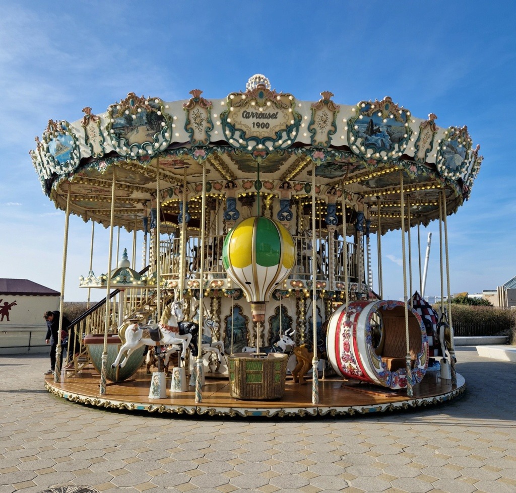 Ornate vintage double-decker carousel with painted horses and decorative top against blue sky