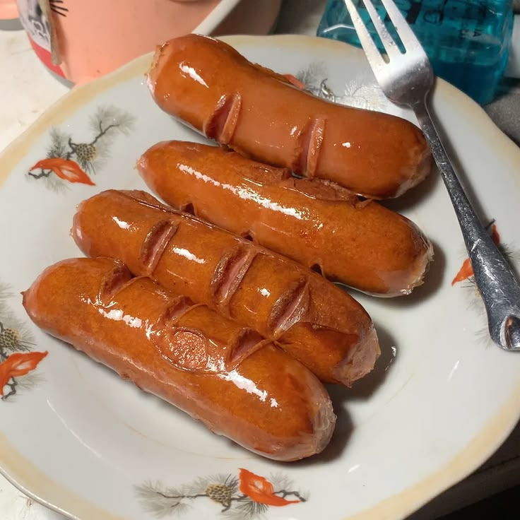 Several browned sausages on a white plate with a fork
