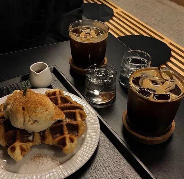 Three iced coffees and waffles with ice cream on black tray with sunlight shadows