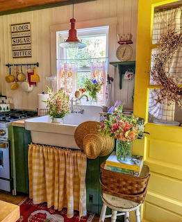 Vintage country kitchen with yellow walls, white sink, gingham curtains, wicker baskets and flowers