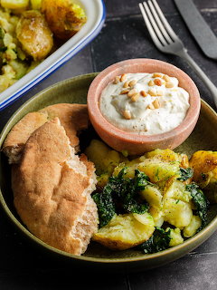 Green plate with pita bread, spinach potato dish, and hummus bowl with pine nuts