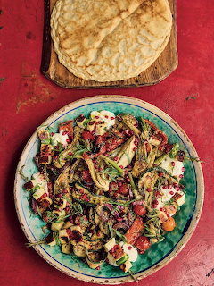 Grilled vegetable salad with cheese on a teal plate next to flatbread on a red surface
