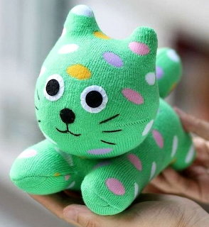 Green stuffed sock cat toy with colorful dots resting on a hand