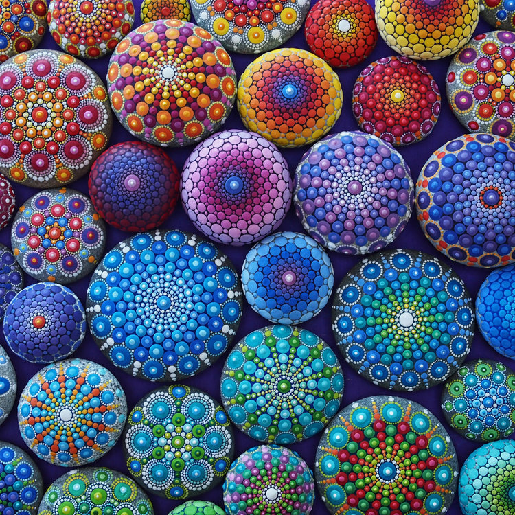 Collection of hand-painted stones with colorful mandala dot patterns in rainbow colors arranged on dark background
