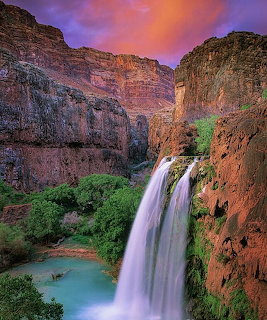 Waterfall flowing into turquoise pool in red rock canyon at sunset