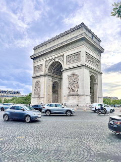 Arc de Triomphe in Paris with cars on a cobblestone street under a cloudy sky