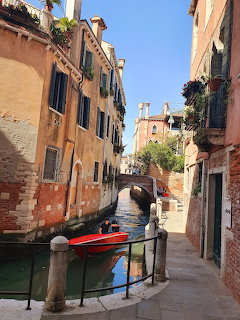 Narrow Venice canal with red boat, old buildings with balconies, and a small bridge in the background