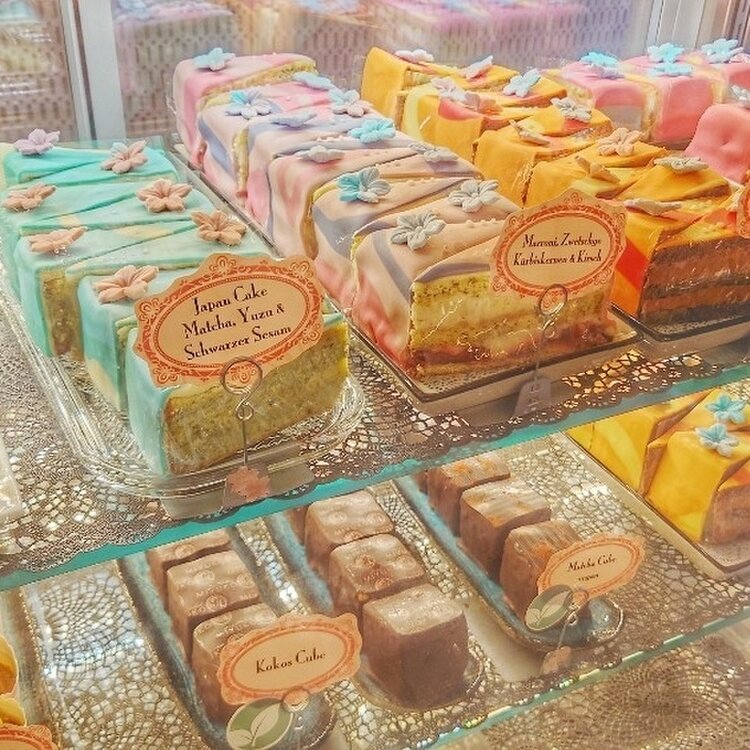 Glass display case with colorful decorated cake slices and petit fours in pastel wrappers with flavor labels
