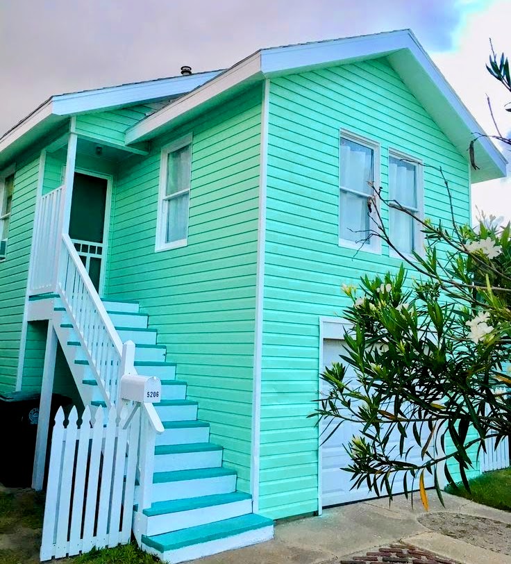 Turquoise and mint green two-story beach house with white wooden stairs and tropical plants