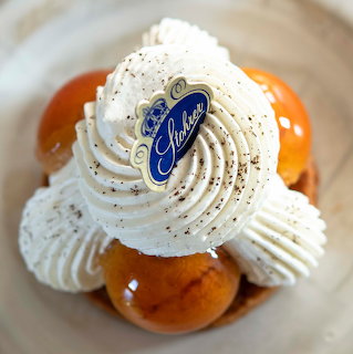 St Honoré pastry with cream puffs, whipped cream swirls, and blue Stohrer label on white plate