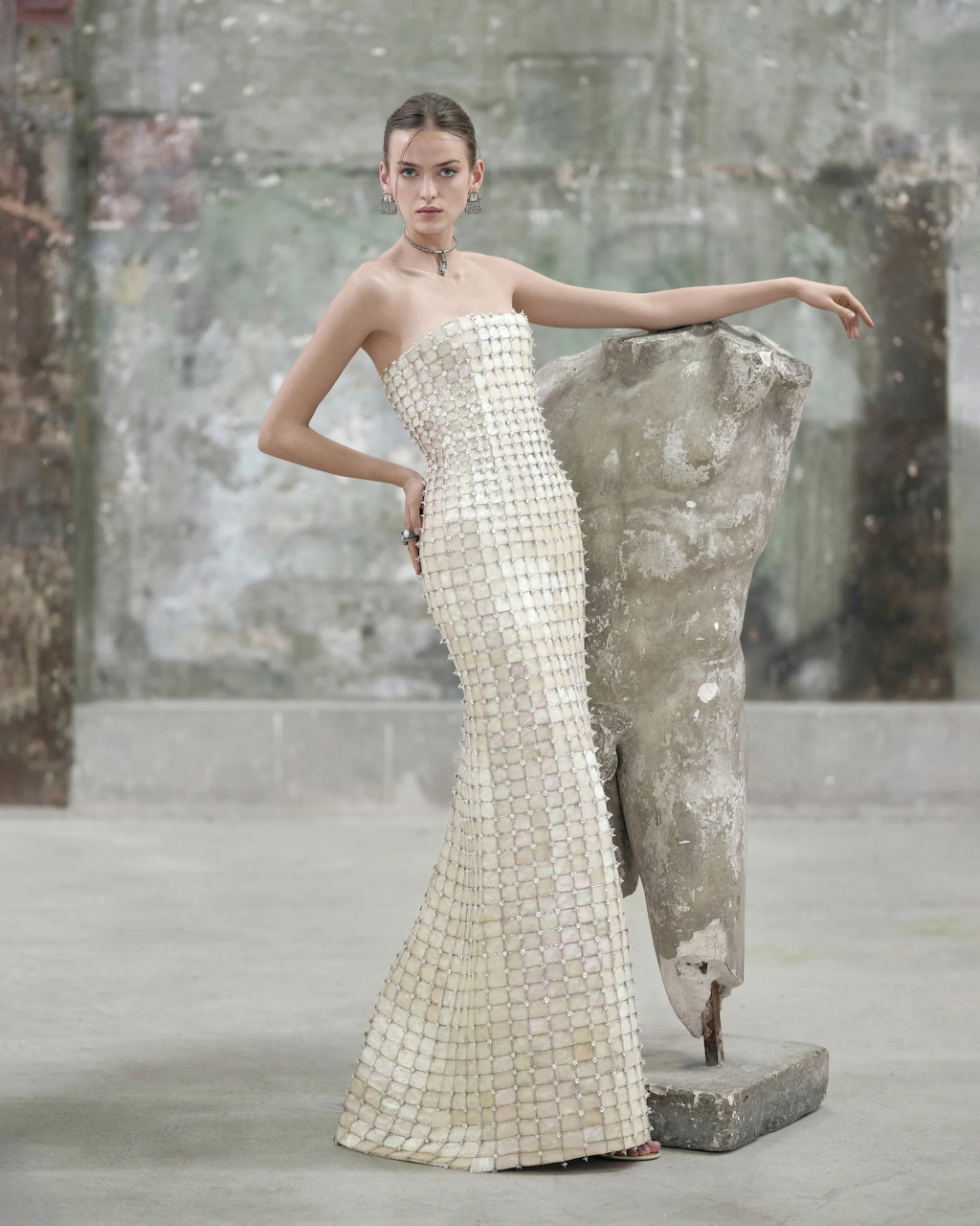 Bride wearing a white pearl-covered gown standing near textured gray concrete wall