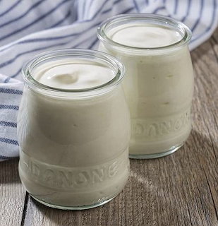 Two glass jars of creamy white yogurt on a wooden table with a striped cloth