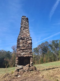 Stone chimney ruin standing alone in a grassy field under a blue sky