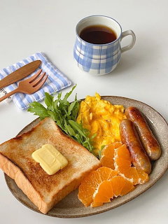 Plate with toast, scrambled eggs, sausages, orange slices, greens, and a mug of tea