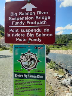 Trail sign at Big Salmon River showing suspension bridge direction and park information board