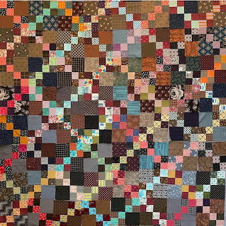 Dense patchwork quilt with colorful fabric squares in various patterns and earth tones