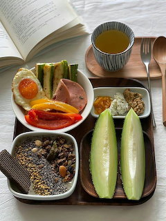 Tray of Korean-style food with bread, fruit, cereal, side dishes, melon, and tea