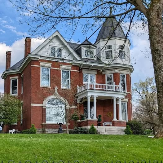 Red brick Victorian house with turret and white porch on green lawn