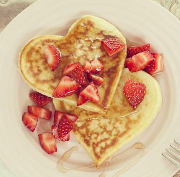 Heart-shaped pancakes garnished with sliced strawberries on white plate