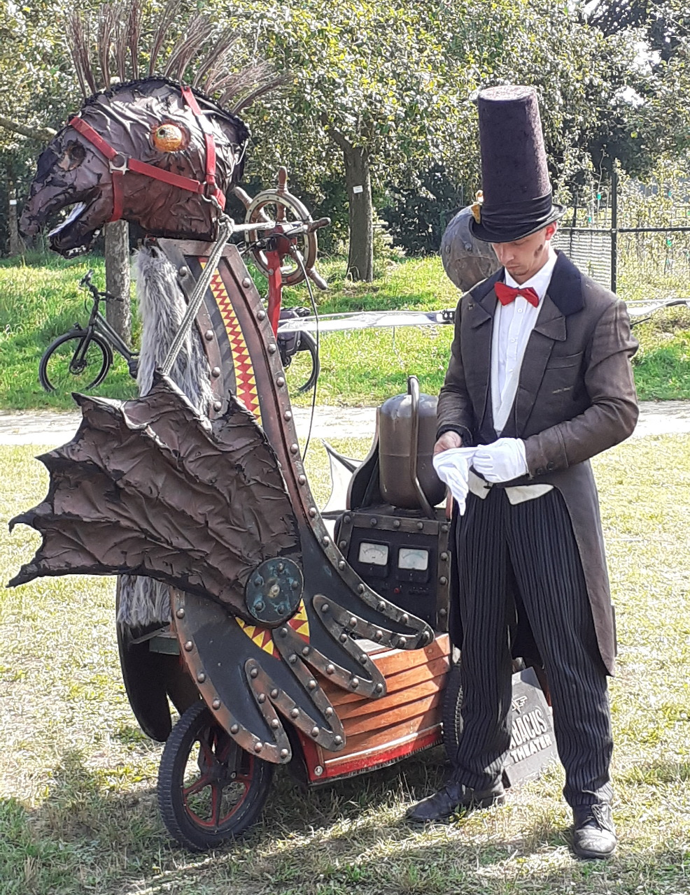 Man in top hat and tuxedo beside a steampunk dragon-shaped vehicle with metallic scales and wings