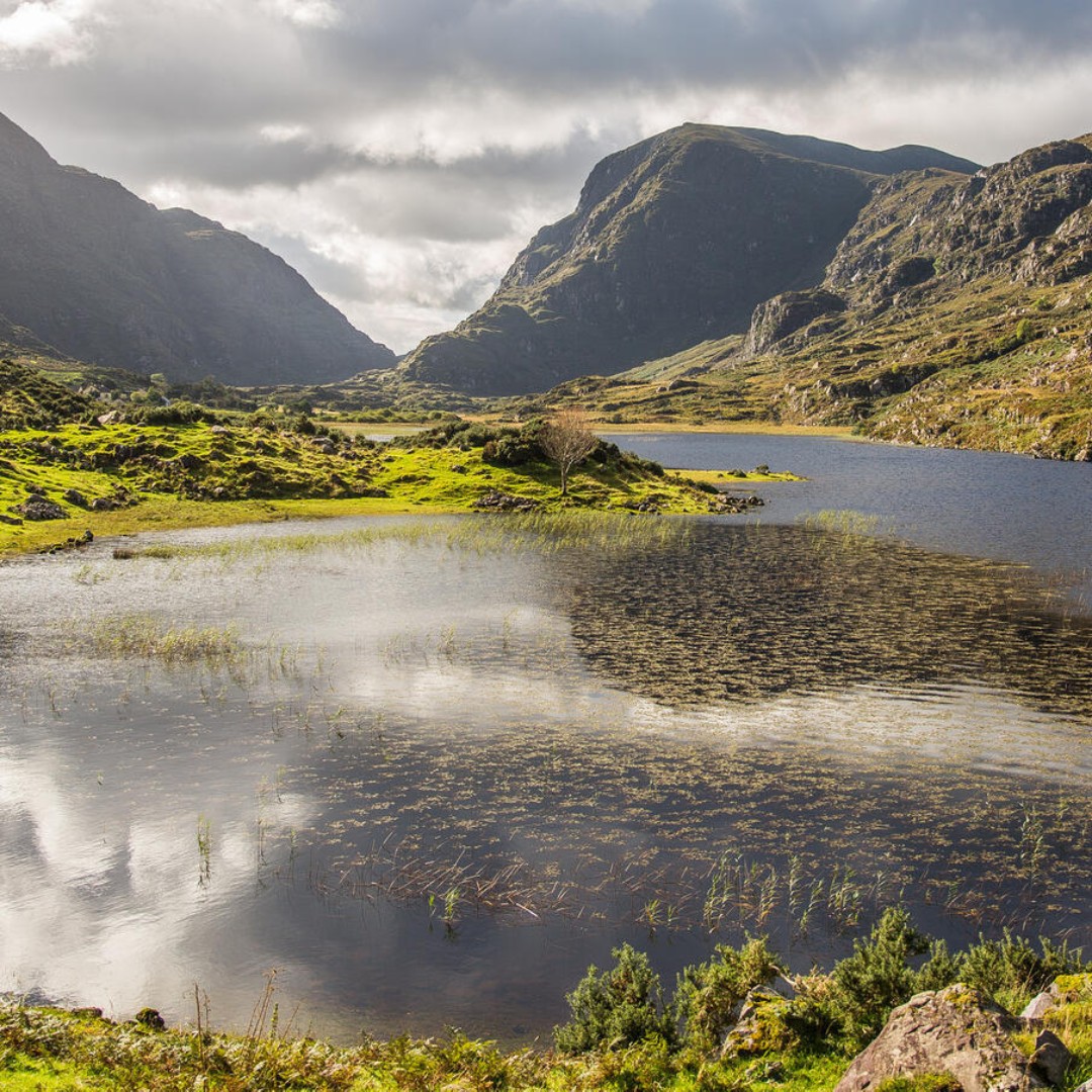 Mountain lake in a rocky green valley under cloudy skies