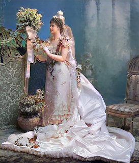 Woman in ornate Victorian bridal gown with floral details holding bouquet in studio setting