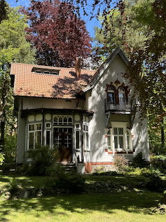 White Victorian cottage with orange roof and arched windows surrounded by tall green trees on a sunny day