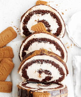 Sliced chocolate Swiss roll cake with cream filling beside biscuits on a white surface