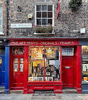 Red storefront of art print shop with brick building facade and large window displaying framed pictures