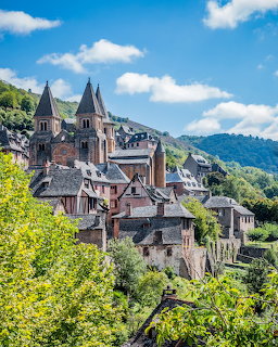 Stone village and church with twin spires on a green hillside beneath a blue sky